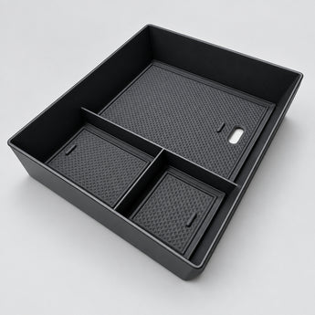 A black plastic drawer organizer insert with three compartments, shown from an elevated angle on a light beige marble surface.