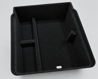 A black molded plastic storage organizer tray with a textured, non-slip surface, shown on a light beige marble countertop.